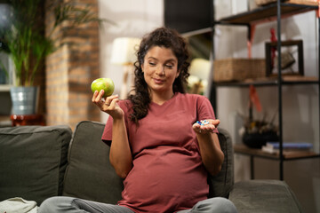 Pregnant woman choosing between pills and fruit.