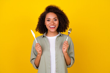 Photo of impressed wavy young brunette lady hold knife folk wear grey shirt isolated on yellow color background
