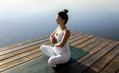 Pregnant woman doing yoga at lake during the day.