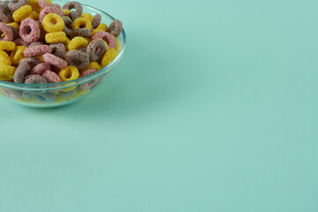 Part of a glass plate with corn rainbow breakfast rings on a turquoise background.