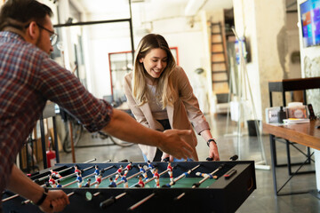 Fototapeta premium Colleagues having fun at work. Businessman and businesswoman playing table soccer