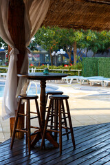 Nobody seat at the wooden stool at the restaurant open air at noon near by a pool.
