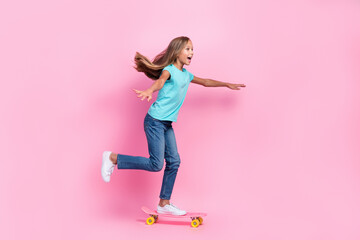 Full length photo of funky impressed little child dressed teal t-shirt riding skateboard empty space isolated pink color background © deagreez