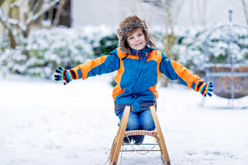 Little kid boy enjoying sleigh ride during snowfall. Happy preschool kid riding on vintage sledge....