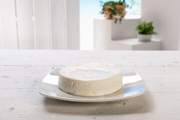 fresh cheese on white plate resting on white wooden table, set