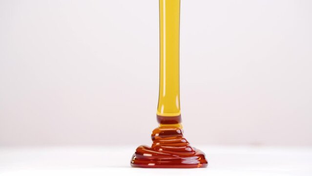 Glob of honey drizzled onto white plate stacking ripples in slow motion back and forth on white studio backdrop in 4k