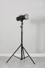 Professional beauty dish reflector on tripod near grey wall in room. Photography equipment