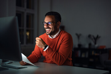 A positive businessman working late at night, talking to someone online.