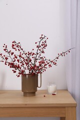 Hawthorn branches with red berries and candle on wooden table indoors