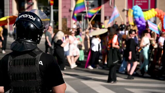 A policeman supervises and secures LGBT protest. LGBTIQ March Pride. Colorful parade celebrating LGBTI rights. Protesters walking with banners and flags. Human rights. 