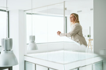 Businesswoman leaning on railing in minimalist office corridor
