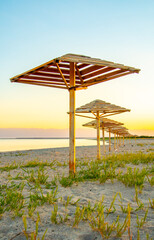 A four-sided umbrella from the sun on the beach made of natural materials, bamboo and reeds against the background of the sea and the sandy shore.