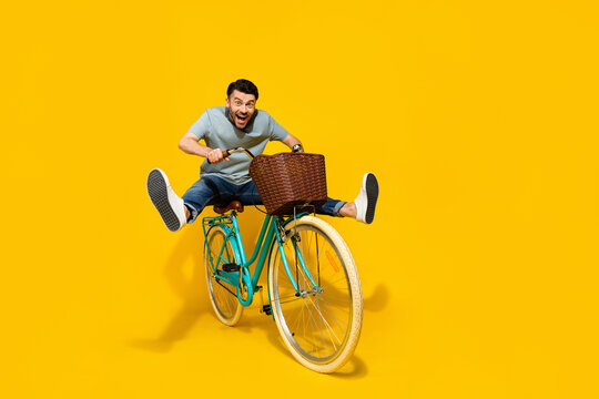 Full length photo of young funky energetic guy riding retro eco bicycle with busket legs up crazy excited isolated on bright yellow color background