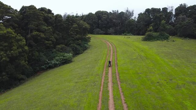 A man Riding his Royal Enfield Himalayan Adventure Motor cycle through the road between a beautifull grass Land in Ooty Mountains , Thamil Nadu , India