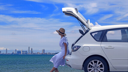 Woman relaxing inside the white hatchback car trunk at the beach and watching to the blue sea with blue sky and white cloud background. Traveler car concept.