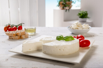 fresh cheese with slice and basil leaf, tomatoes, olive oil, on white square plate, placed on a white wooden table