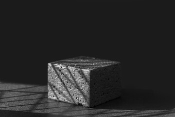 Black square geometric platform in sunlight with shadows. Concept of 3d podium for presentations of packaging and cosmetics. Close-up, copy space, monochrome image