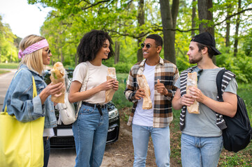 Group of young people in the forest standing near the car and eating sandwiches