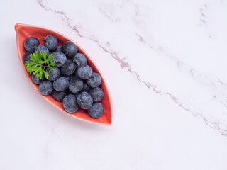 Top view, fresh blueberries in leaves-shaped red plate on grey background. Flat lay with copy space. Concept for healthy eating and nutrition, Superfood..