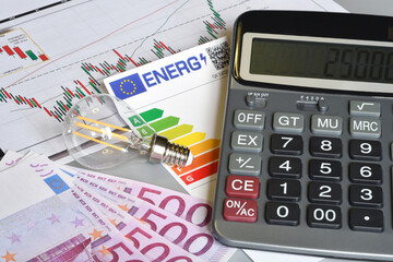 Close up of light bulb, calculator and energy efficiency rating table over 500 euro banknotes. Concept for the rising cost of electricity. Expensive energy bill and rising electricity prices.