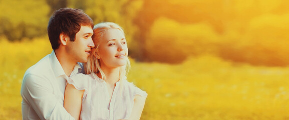 Close up portrait of happy lovely young couple sitting on the grass together looking away on sunny...