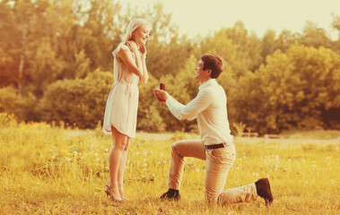 Happy young couple, man kneeling down and proposing a ring to his beloved woman outdoors in the...