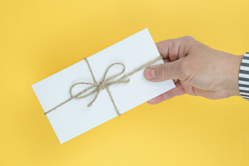 Man holding in the palm of his hand white paper envelope tied with a rough rope on a bright yellow background. The concept of a postal item, an unexpected surprise and a congratulation.