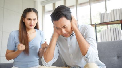 Young asian couple mad at each other in their home. Disgruntled man sitting on couch with his...