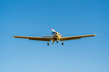 Single-propeller plane landing from a front view into a blue sky
