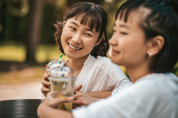 Two asian young girls having good time together and drinking lemonade