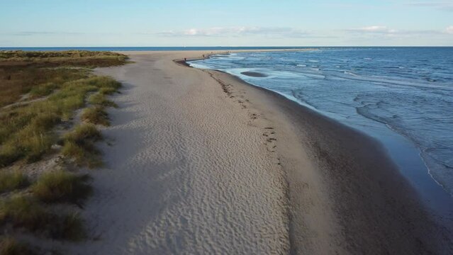Drone view of the beautiful beach covered in grass under the blue cloudy sky in Skagen, Denmark