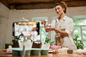 Young beautiful girl culinary specialist writes video blog on baking. Smiling female vlogger or shooting blog filming reportage advertising video