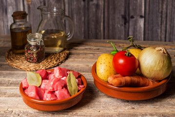 Ingredients for a beef stew,pieces of beef,potatoes,onions,peppers,carrots,tomatoes,oil,laurel and white wine,on an old wooden table.