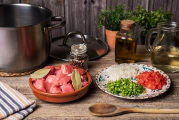 Ingredients next to a pot for a beef stew, pieces of beef, white wine and chopped vegetables for...