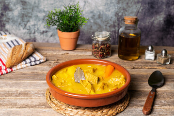 Rustic clay dish with stewed beef, along with bread, oil, pepper and salt, on an old wooden table. Close-up.