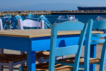 Closeup on wooden table and chair in typical fish tavern at fishing port. Selective focus. Big ship on background. Aegean island Chios in Greece on an autumn day. Greek holidays and destinations