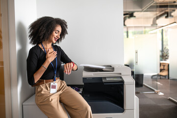 Curly-haired young woman near xerox in the office waiting for somebody