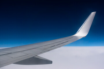 View from the plane window to the wing. Photo taken while flying above the clouds. In the distance, a visible horizon made of clouds