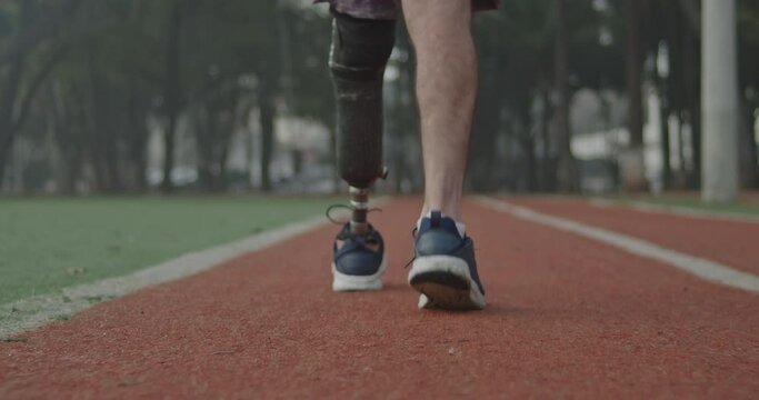 Back view of a disabled athlete man with prosthetic leg walking on running track