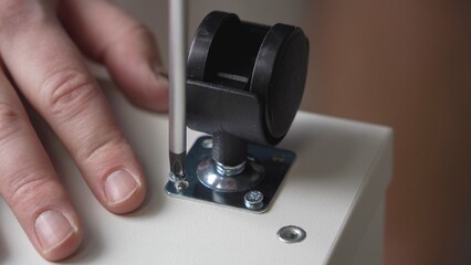 Male hands with a screwdriver screw the fittings to the furniture with a screw.