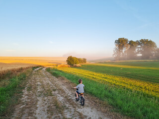 Little boy riding bike in countryside. Riding person at sunset in nature. Child spending his free time active. Freedom, beautiful landscape. Happy childhood.