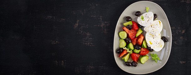 Greek salad of fresh cucumber, tomato, burrata cheese and black olives with olive oil. Healthy food. Top view, banner