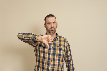 Handsome 40 years old man over isolated beige background looking unhappy and angry showing rejection and negative with thumbs down gesture. bad expression