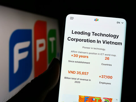 Stuttgart, Germany - 10-01-2022: Person holding smartphone with website of Vietnamese IT company FPT Corporation on screen in front of logo. Focus on center of phone display.
