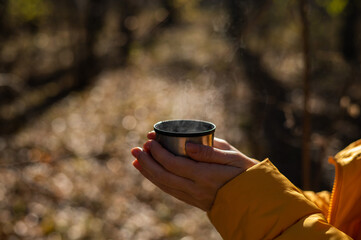 A woman holds a thermos of hot tea in her hands on a cold autumn day.