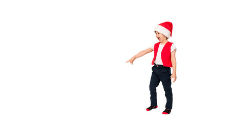 Portrait of standing surprised child in red Santa Claus hat point finger out on something. Isolated on white background. 5 year European boy. Banner. Copy space. Christmas time and New Year concept