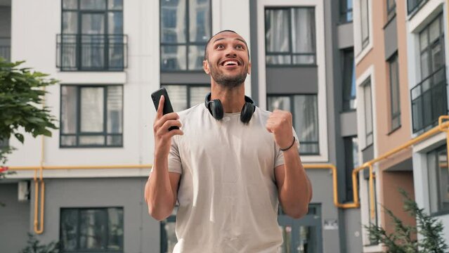 Excited african american man standing outdoors reading email on phone with good news receiving great offer job promotion winning lottery receives cash prize celebrating victory rejoicing in success.