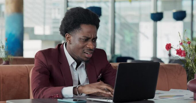 A young businessman in a suit works in front of a laptop in a restaurant. Heartbroken man can't find saved documents, laptop crashes.