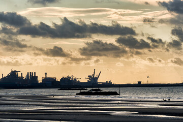 Obraz premium low tide and a steelworks in silhouette and port with loading cranes and containers of the port of Dunkirk, France