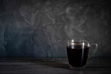 Black hot americano coffee with steam in clear cup on wooden desk with  dark loft style walk  background